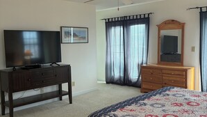 Een slaapkamer met een bed, een dressoir, een televisie, een plafondventilator en een raam met gordijnen.