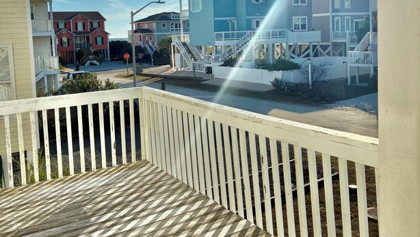Een houten terras met een balustrade, uitzicht op een woongebied met huizen, en een heldere lucht.