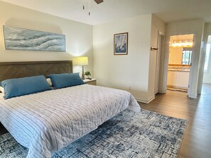 A bedroom with a bed, a nightstand, a lamp, a painting, and a view of the kitchen. - 4BR retreat with dock overlooking the ICW (Holden Beach)