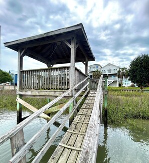 A wooden pier leading to a covered area with a view of houses in the background. - 4BR retreat with dock overlooking the ICW (Holden Beach)
