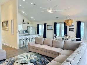 Ein modernes Wohnzimmer mit einem Ecksofa, einem Glastisch und einem Essbereich mit weißen Stühlen und einem Tisch.