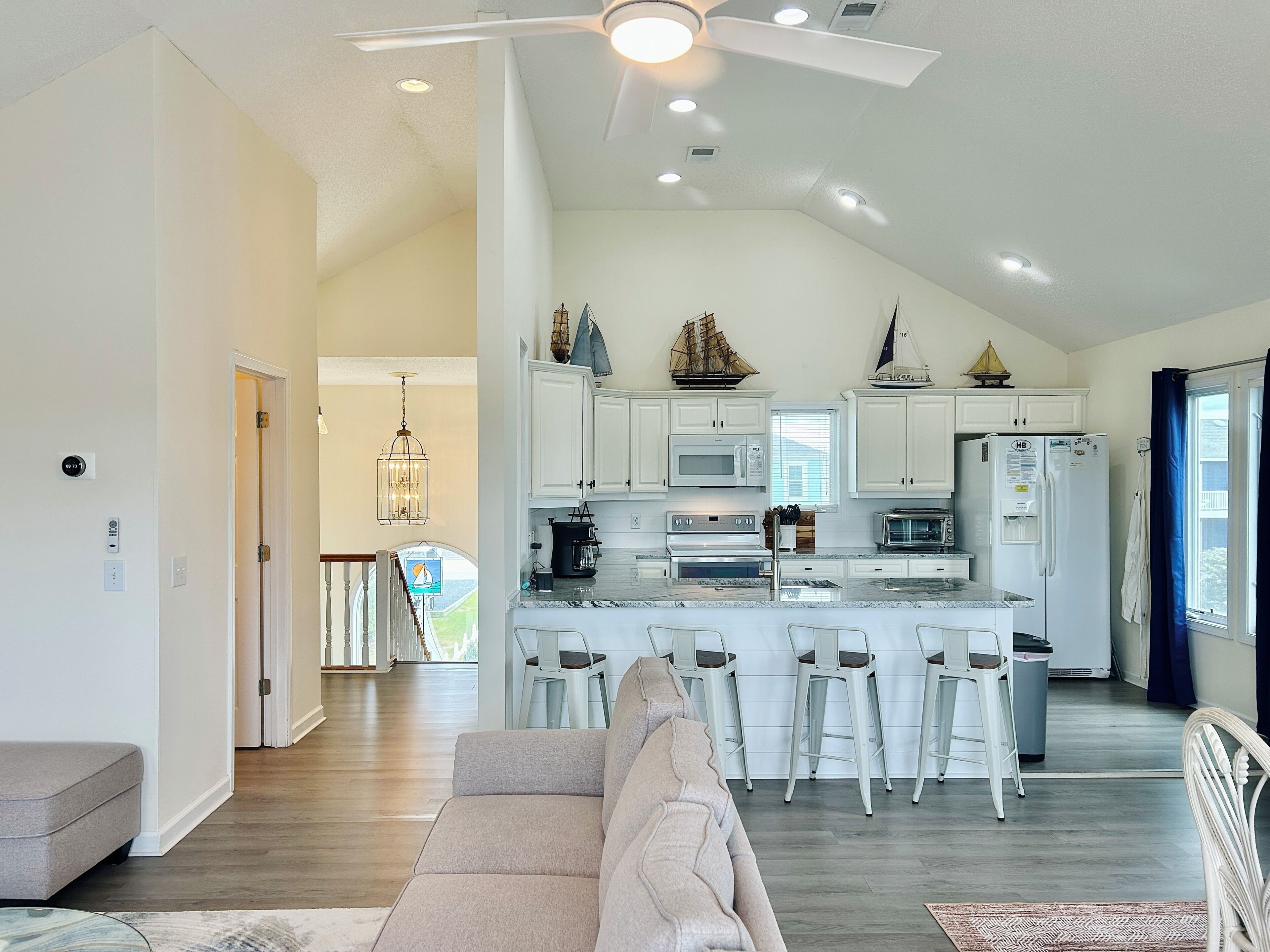 A modern kitchen with white cabinets, a central island, bar stools, and a ceiling fan.