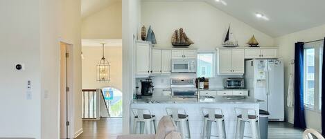 A modern kitchen with white cabinets, a central island, bar stools, and a ceiling fan.