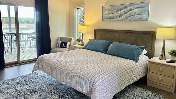 Een slaapkamer met een bed, twee bedlampen, een nachtkastje, een stoel, een raam en uitzicht op het landschap.