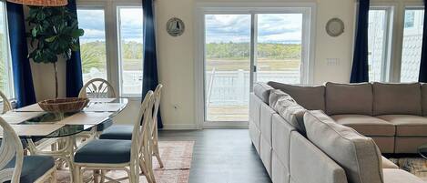 Ein großzügiger Wohnbereich mit Sofa, Esstisch, Stühlen und Blick ins Freie durch eine Glastür.
