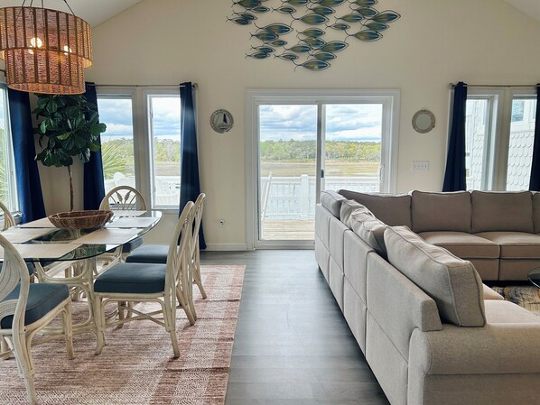 Ein großzügiger Wohnbereich mit Sofa, Esstisch, Stühlen und Blick ins Freie durch eine Glastür.