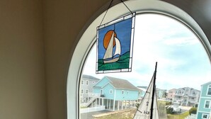 Een kamer met een groot rondboogvenster dat uitkijkt op een woongebied, een klein modelzeilbootje en een decoratieve glas-in-loodraming.