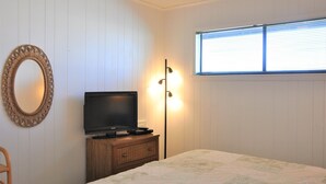 Una camera da letto con televisione, abat-jour, specchio e finestra con persiane.