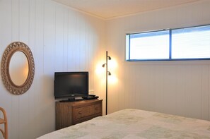A bedroom with a television, a bedside lamp, a mirror, and a window with blinds. - Oceanfront 3BR, 2BA Holden Beach getaway (Holden Beach)