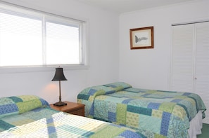 Een slaapkamer met twee bedden, een nachtkastje, een lamp, een ingelijst schilderij en een kast.