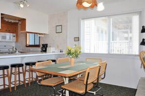 Een keuken met een eethoek, met een tafel met stoelen, een koffiezetapparaat en een klok aan de muur.