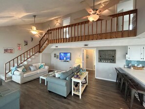 A spacious living area with a staircase, a television, and a kitchen area. - 4BR, 2BA Holden Beach retreat located on the 2nd row (Holden Beach)