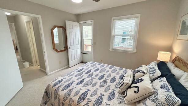 A bedroom with a bed, a ceiling fan, a window with blinds, and a door. - 4BR, 2BA Holden Beach retreat located on the 2nd row (Holden Beach)