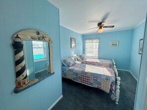 Ein Schlafzimmer mit einem Bett, einem Deckenventilator, einem Fenster mit Jalousien und einem Wandspiegel.