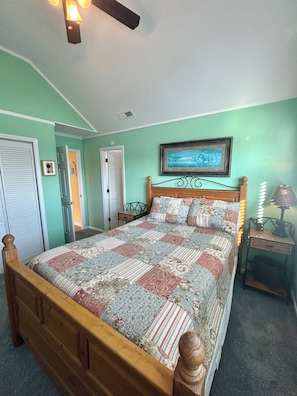 A bedroom with a wooden bed, a ceiling fan, a framed picture on the wall, and a nightstand with a lamp. - "Courtside" cozy 4 bedroom home, short walk to the Beach!! (Holden Beach)