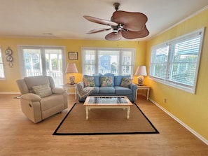 A living room with a beige armchair, a blue sofa, a coffee table, and a ceiling fan. - "Courtside" cozy 4 bedroom home, short walk to the Beach!! (Holden Beach)