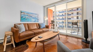 Uma sala de estar moderna com um sofá de couro marrom, uma mesa de centro de madeira e uma janela grande com vista para um edifício.
