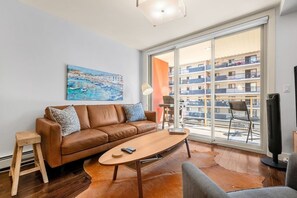 Ein modernes Wohnzimmer mit einem braunen Ledersofa, einem Holztisch und einem großen Fenster mit Blick auf ein Gebäude.