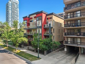 A multi-story residential building with balconies, a parking area, and a clear sky. - Sage & Saddle | Balcony | UG Park | Beltline | BBQ (Calgary)