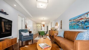 Uma sala de estar moderna com uma televisão de tela plana, um sofá de couro, uma poltrona azul e uma mesa de centro com livros.