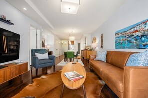 Ein modernes Wohnzimmer mit Flachbildfernseher, einer Ledersofa, einem blauen Sessel und einem Couchtisch mit Büchern.