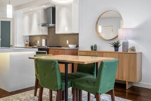 A modern kitchen with white cabinets, a central island, and a dining area with green upholstered chairs. - Sage & Saddle | Balcony | UG Park | Beltline | BBQ (Calgary)