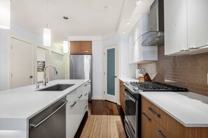 A modern kitchen with stainless steel appliances, white cabinetry, and a wooden backsplash. - Sage & Saddle | Balcony | UG Park | Beltline | BBQ (Calgary)