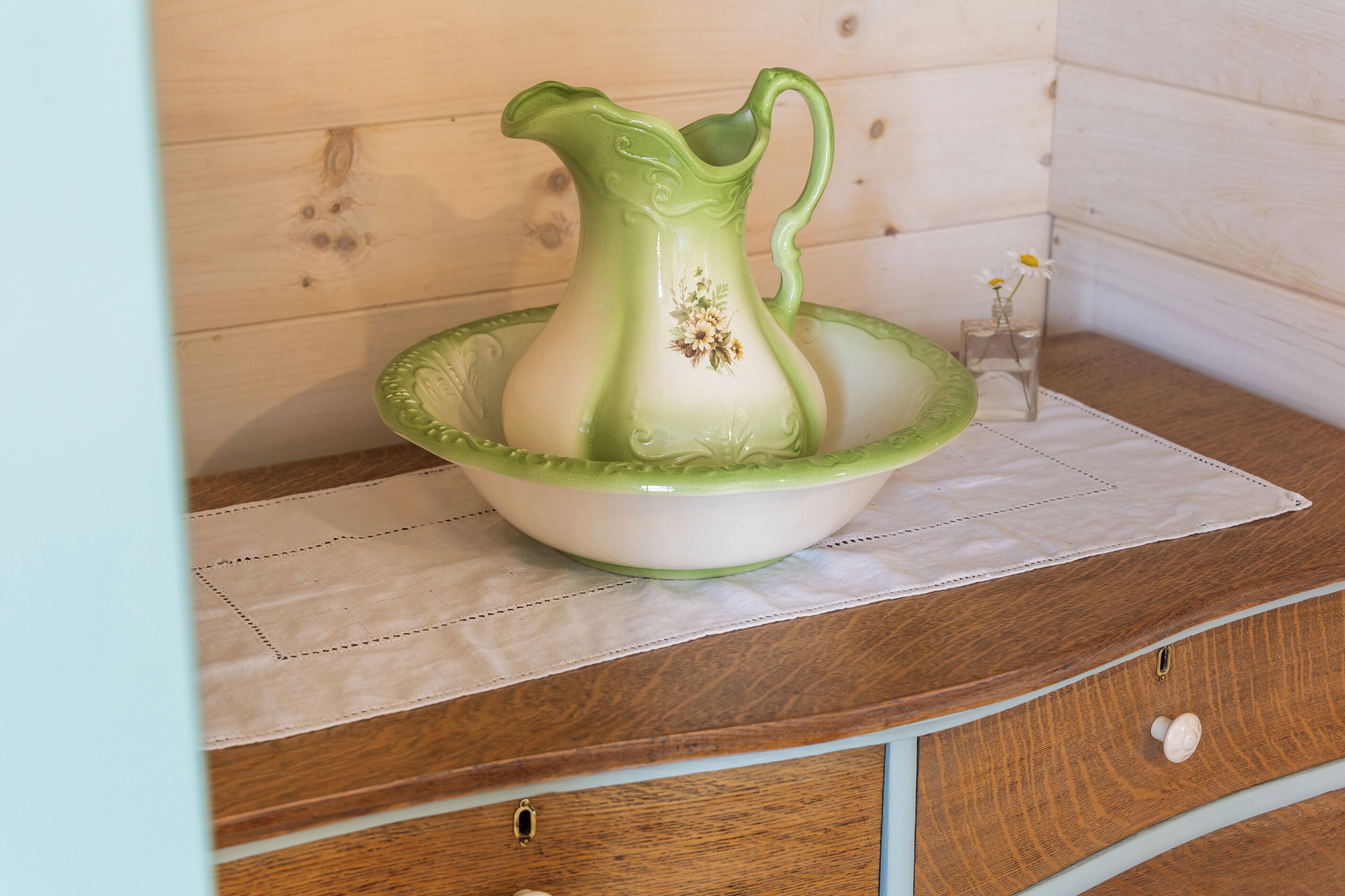 Een groene keramieken kruik in een witte schaal, geplaatst op een houten ondergrond met een witte doek eronder.
