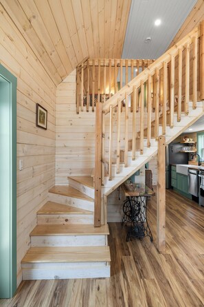 A wooden staircase leading to an upper level, a kitchen area with wooden cabinets, and a small table with a vase.