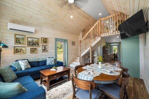 A wooden interior with a sofa, dining table, chairs, and a staircase.