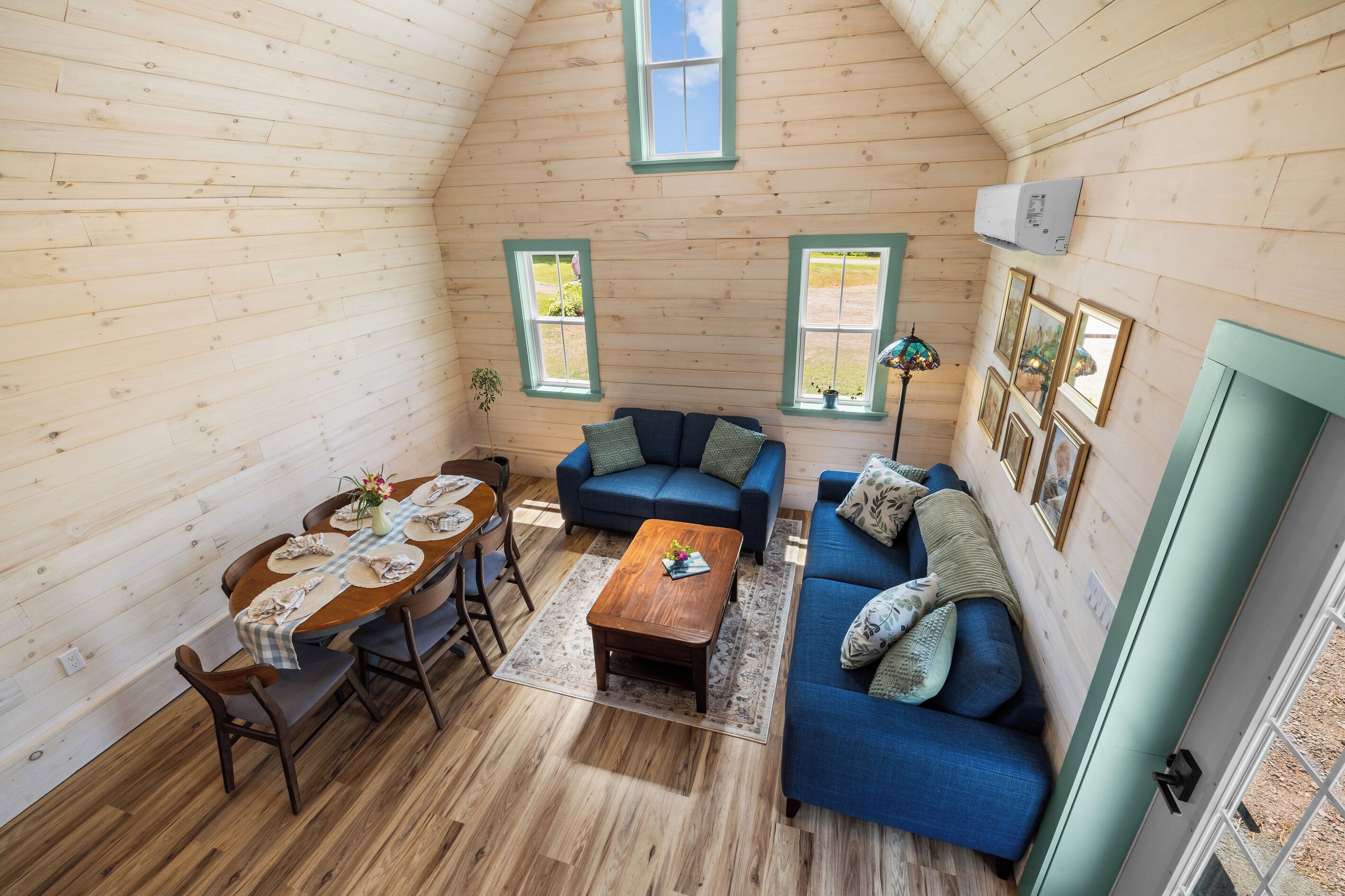 A cozy room with wooden walls, a dining table with chairs, a blue sofa, and a small wooden coffee table.