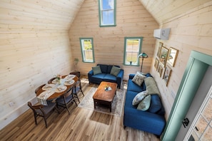 Una habitación acogedora con paredes de madera, una mesa de comedor con sillas, un sofá azul y una pequeña mesa de centro de madera.
