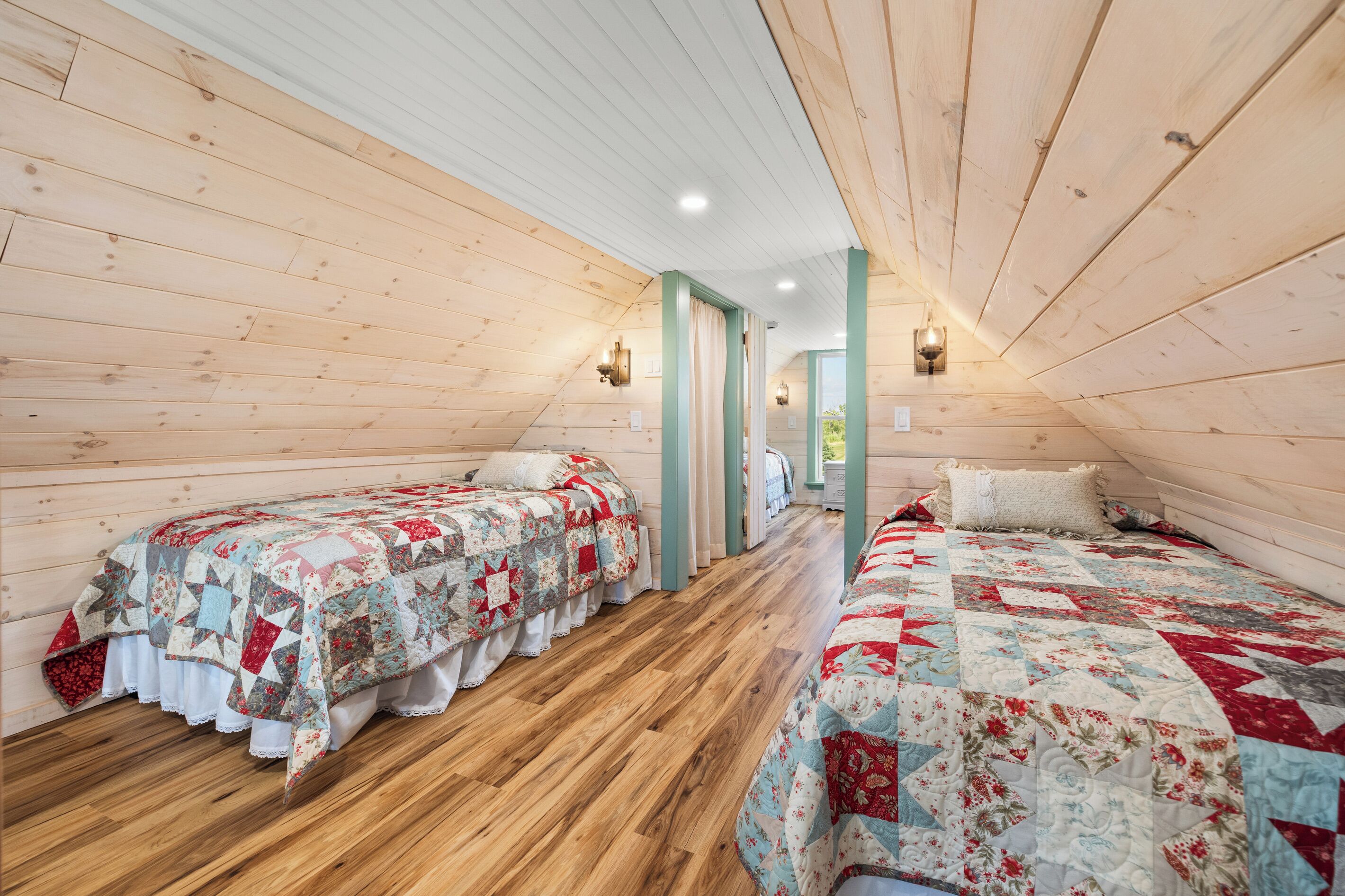 Un dormitorio de buhardilla acogedor con paredes de madera, dos camas con colchas, suelo de madera y un tragaluz.