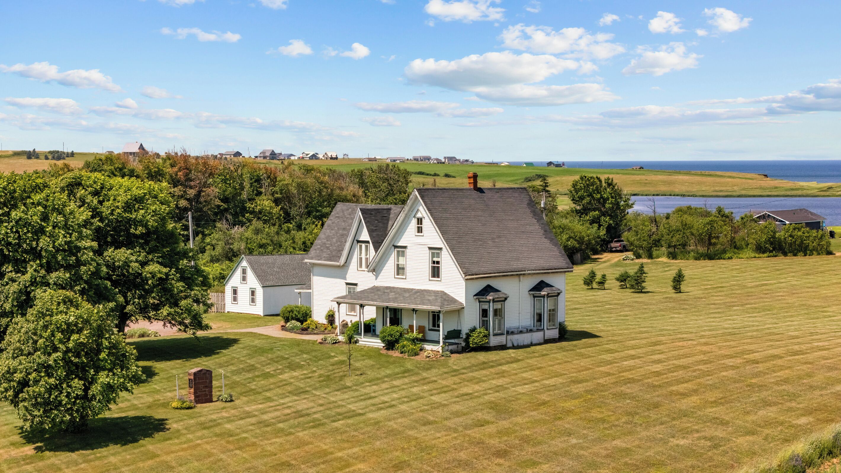 A large white house with a dark roof, surrounded by a well-maintained lawn and a body of water in the background.