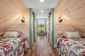 A room with two beds, a wooden floor, a window with a view, and a door leading to another room.