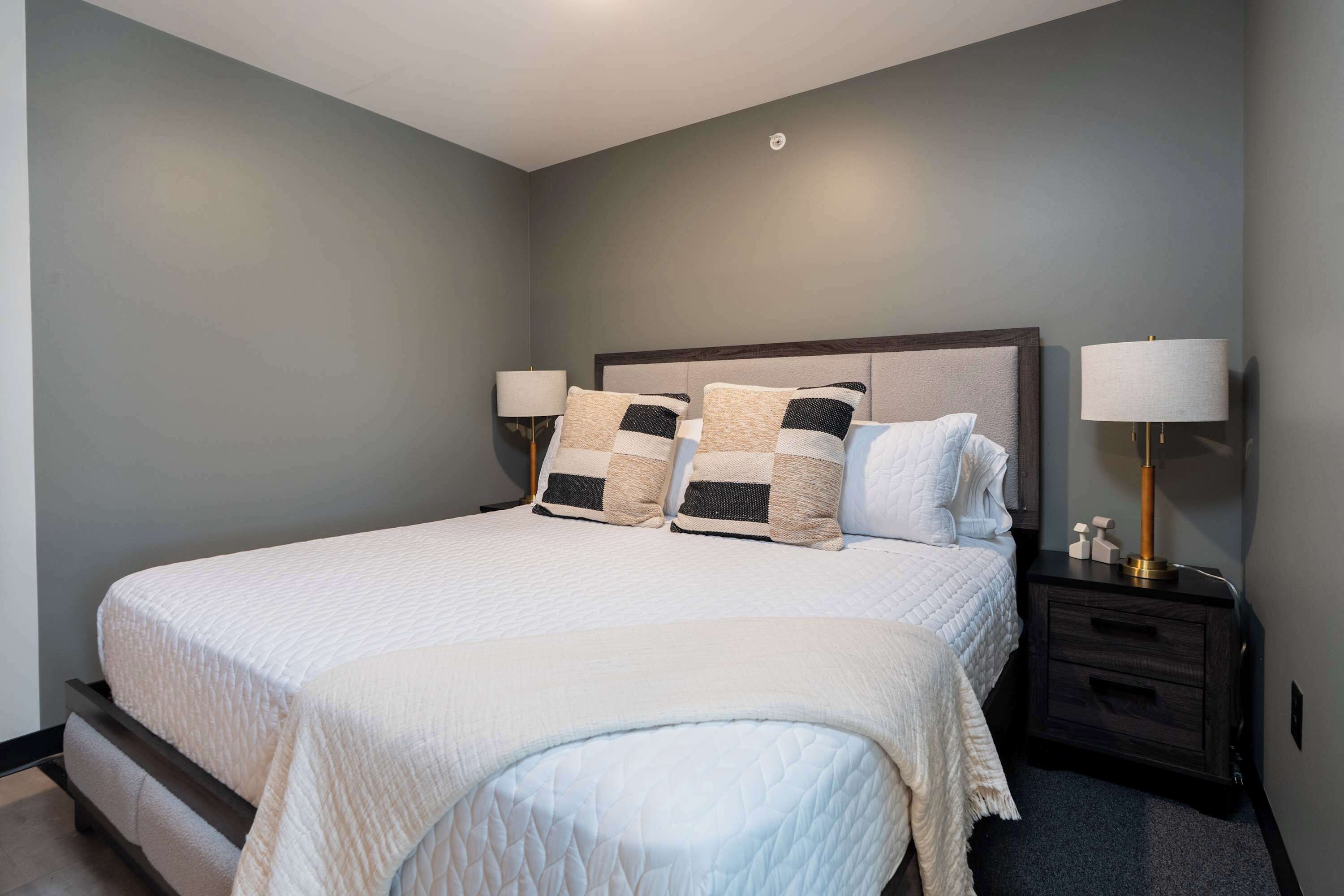 A neatly made bed with a white quilt, two bedside tables with lamps, and a dark wood headboard.