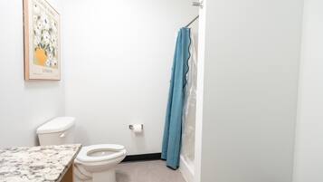 A bathroom with a toilet, a shower curtain, and a marble countertop.