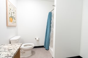 A bathroom with a toilet, a shower curtain, and a marble countertop.