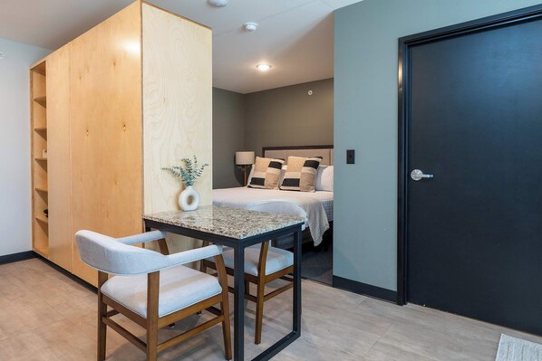 A compact bedroom with a bed, bedside table, and a small seating area with a chair and table.