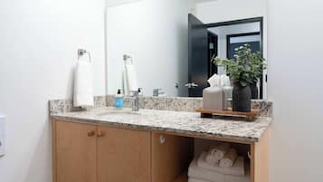 A bathroom with a granite countertop, a sink, a mirror, and a wooden cabinet with towels.