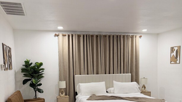Een moderne slaapkamer met een bed, een bruine bank, een potplant en een vloer van marmer.