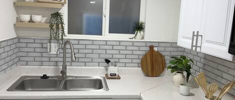A modern kitchen with white cabinets, a double sink, a window, and a stove.