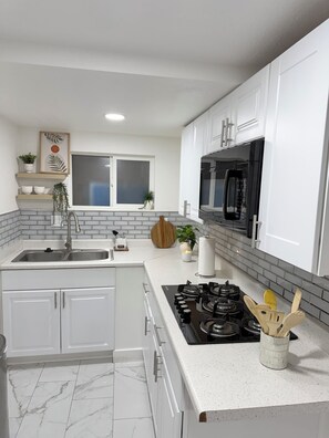 A modern kitchen with white cabinets, a black microwave, a gas stove, and a window with blinds. - Beautiful luxury apartment just 10 minutes from the Strip (Las Vegas)