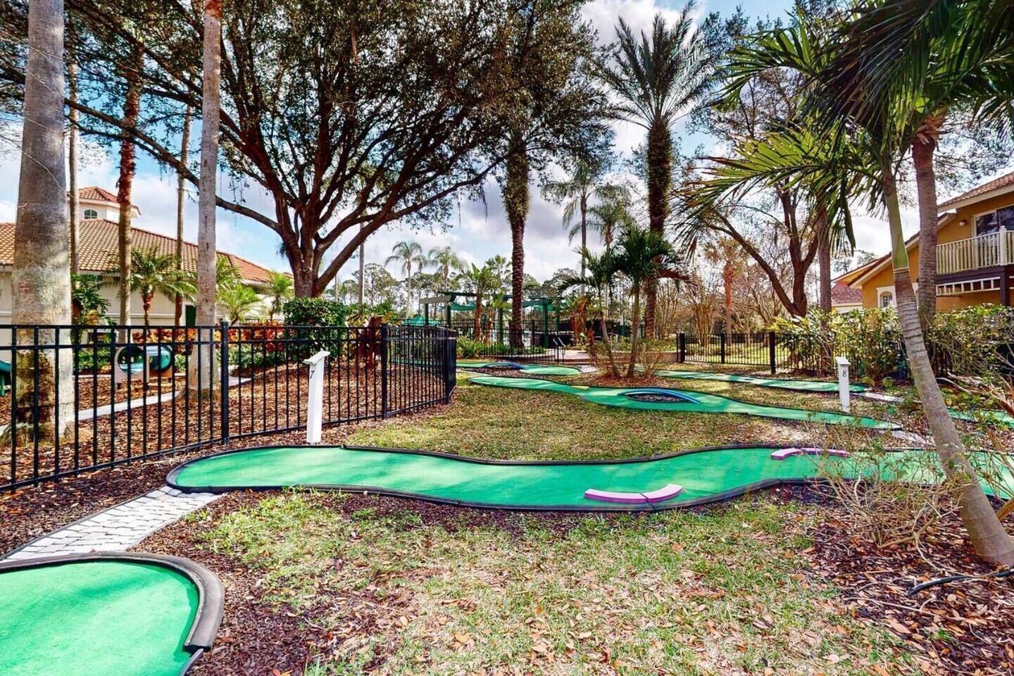 A miniature golf course with multiple holes, surrounded by trees and a fence.