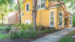 A yellow house with a number 8447, surrounded by greenery and a sidewalk. - Whimsical Couple's Escape: Minutes to Disney (Kissimmee)