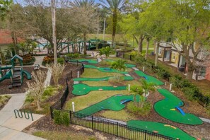A miniature golf course with a green pathway, palm trees, and a playground. - Whimsical Couple's Escape: Minutes to Disney (Kissimmee)