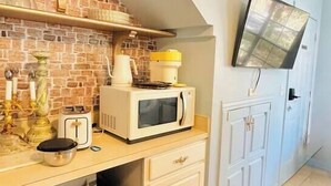A compact kitchen with a microwave, toaster, and refrigerator. A television is mounted on the wall, and a brick-patterned backsplash is visible. - Whimsical Couple's Escape: Minutes to Disney (Kissimmee)