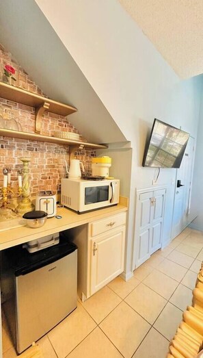 Eine kompakte Küche mit Mikrowelle, Toaster und Kühlschrank. Ein Fernseher ist an der Wand angebracht, und eine Wandfliese mit Ziegeloptik ist sichtbar.