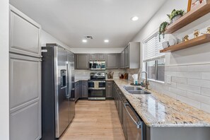 Una cocina moderna con electrodomésticos de acero inoxidable, piso de madera y encimera de granito.