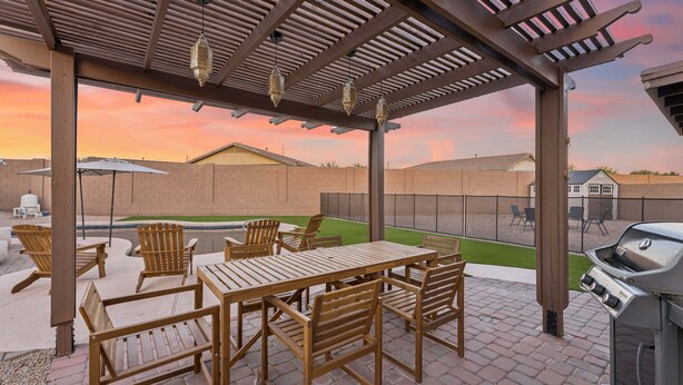 A covered patio with a grill, wooden furniture, and a view of the backyard. - Oasis on Aubrac | Modern 5BR | Private Pool | Pergola & Firepit | Sleeps 8 (San Tan Valley)